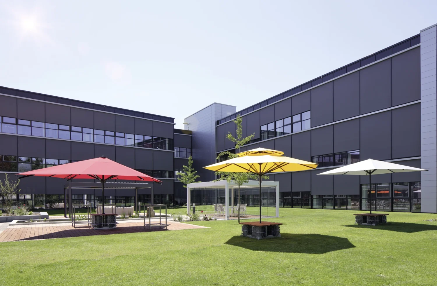 Moderne Bürogebäude mit farbenfrohen Sonnenschirmen auf grünem Rasen